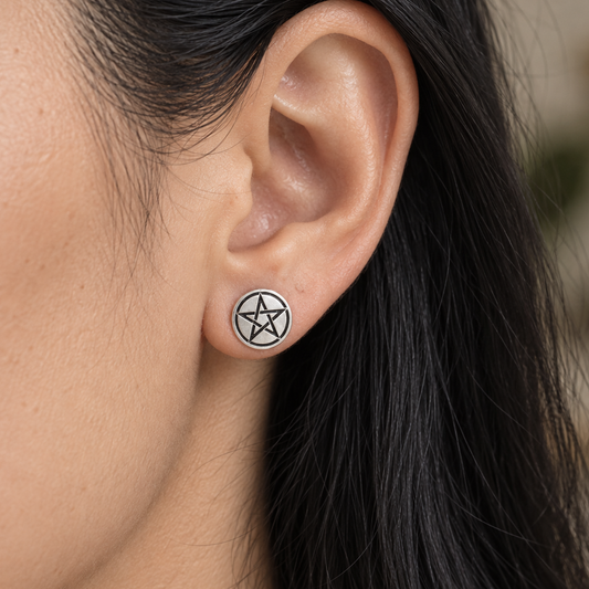 A close-up of a person's ear wearing a small circular earring with a black pentagram symbol on a silver-toned background.