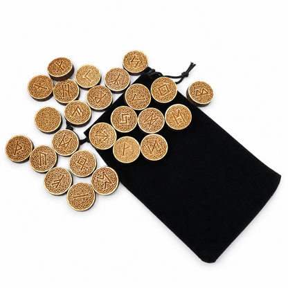 A set of round engraved wooden runes  scattered next to a black velvet drawstring pouch on a white background.